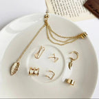 Gold jewelry set including necklaces and earrings on a white plate with a wooden block and paper in the background.
