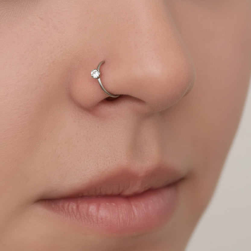 Close-up of a person wearing a silver nose ring on a neutral background