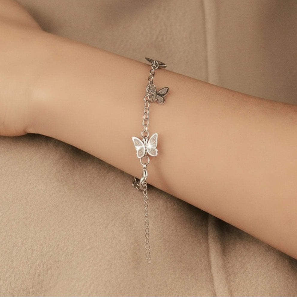 Silver bracelet with butterfly charm on a wrist against a beige background