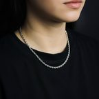 Person wearing a silver chain necklace against a black background