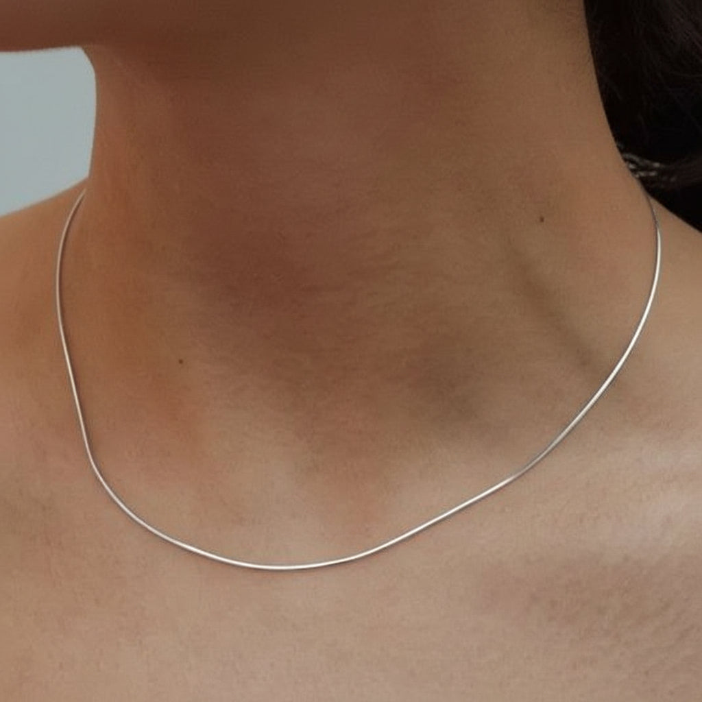 silver necklace on a person's neck against a neutral background