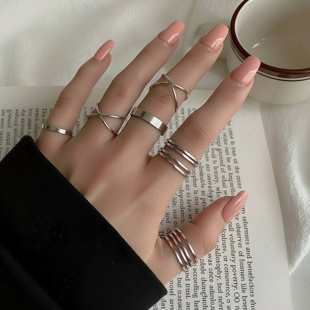 Hand wearing multiple silver rings with red nail polish on a white surface with text.