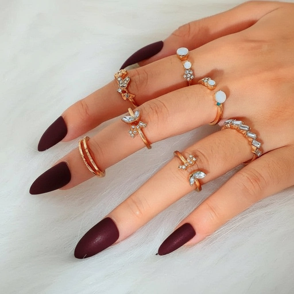 Hand wearing multiple rings with plum nail polish on a light background